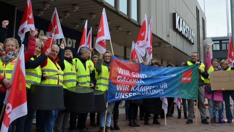 Bild von Streikenden mit Warnwesten und Trommeln vor dem Galeria Kaufhof mit einem Banner "Wir sind Galeria - wir kämpfen für unsere Zukunft"